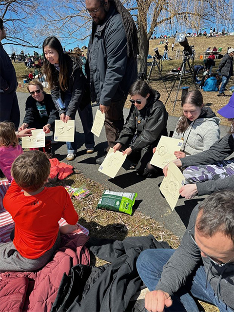 Five Landmark College students play an accessible game with lithographs representing past eclipses provided through the NASA PUNCH Outreach program.